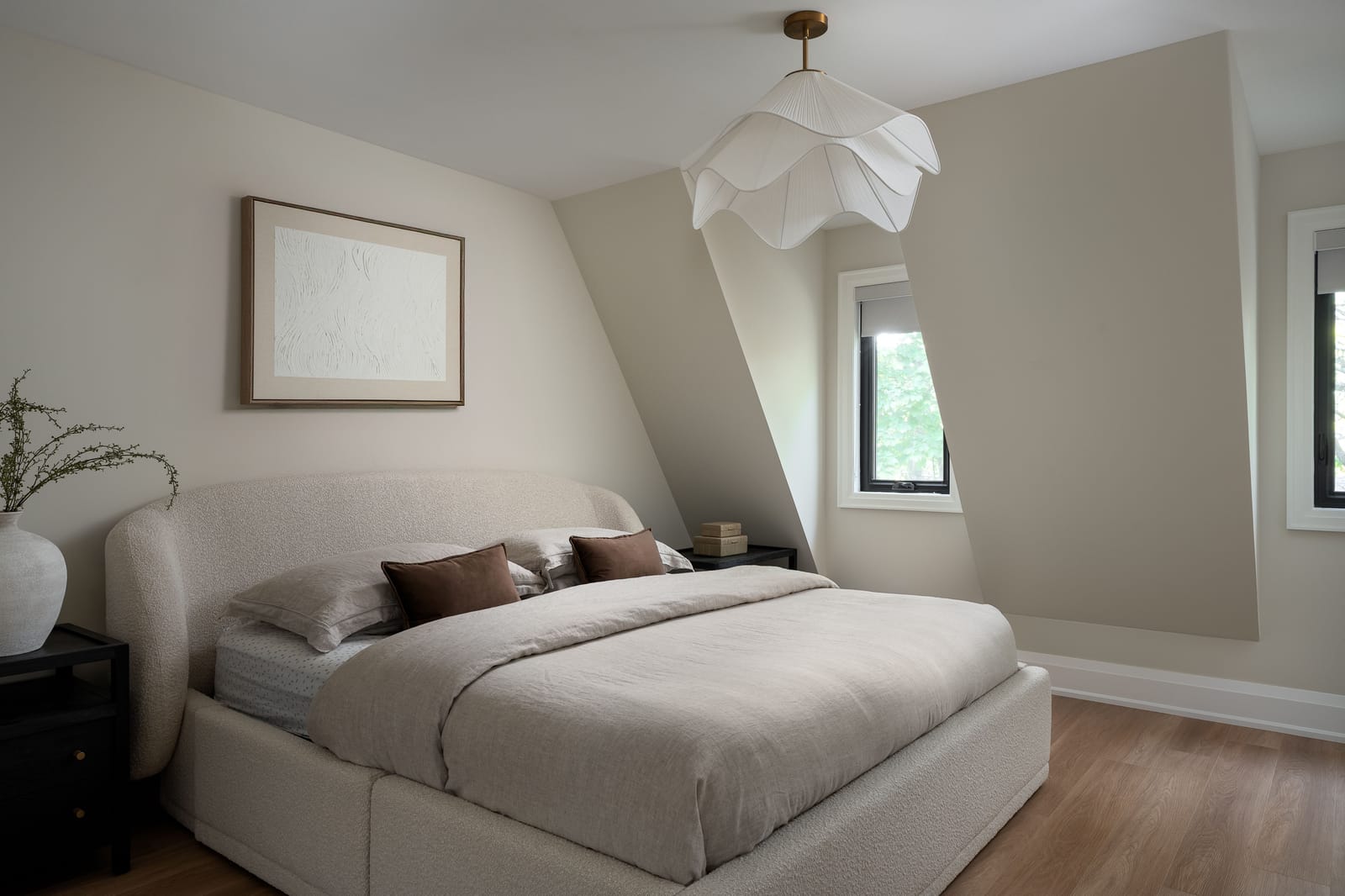 A bedroom with sloped walls following the roof line, a boucle upholstered bed, a paper petal pendant and an oak floor